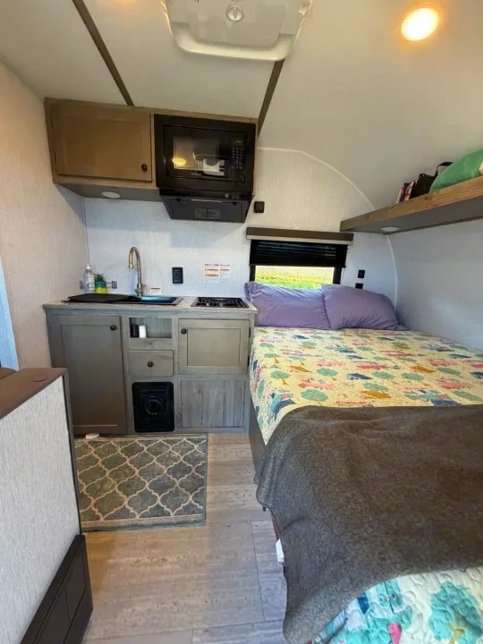 Kitchenette with sink, stovetop, microwave, and bed with floral bedding beyond