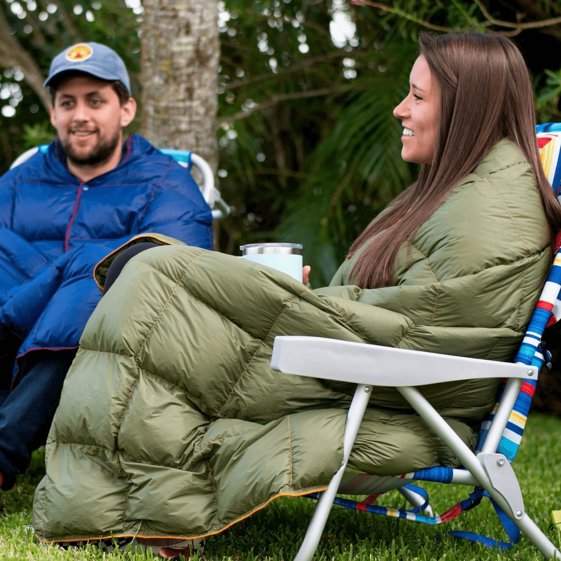 Two campers wrapped in quilted down blankets in camp chairs