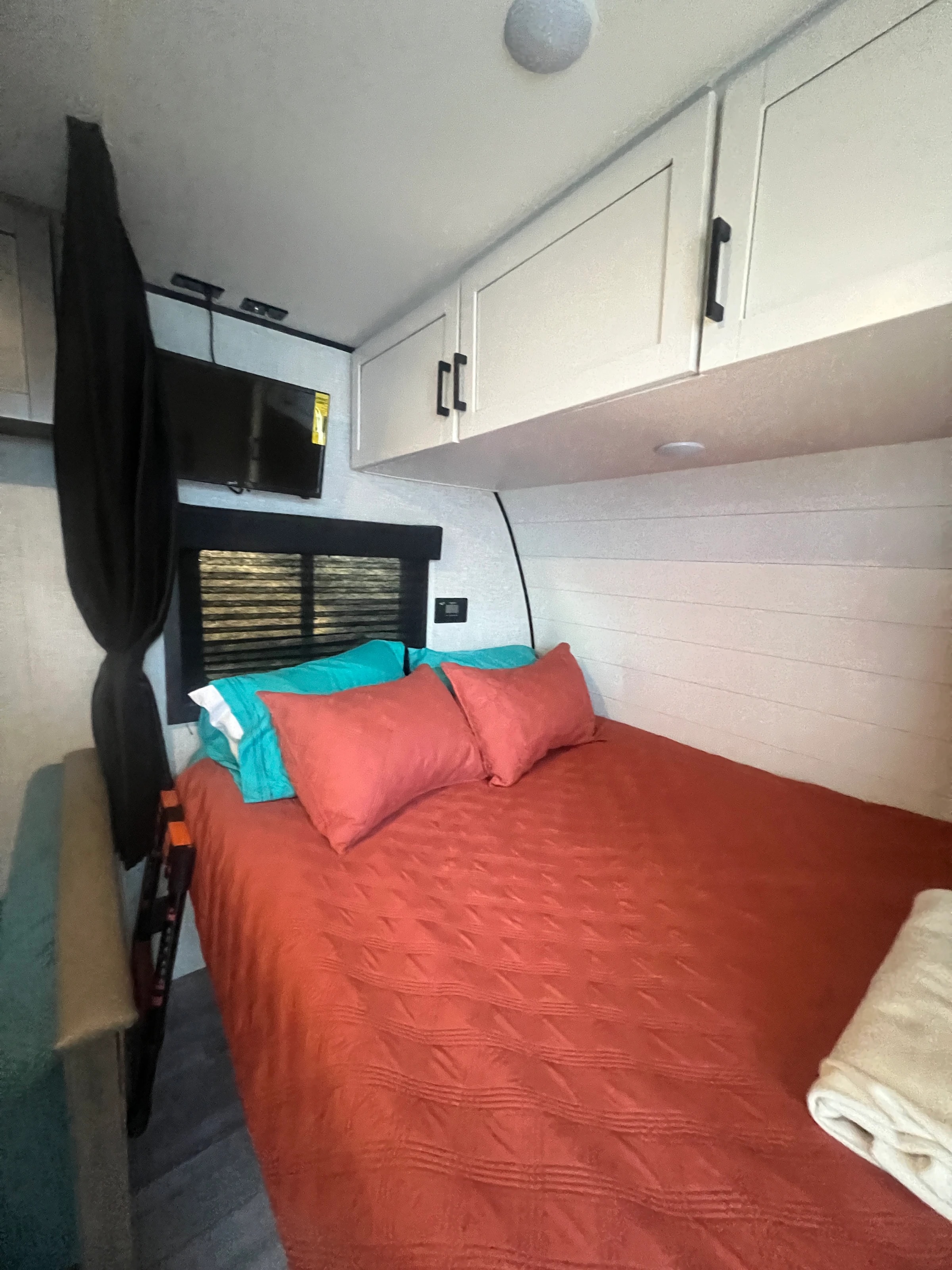 Front queen bed made up with a red quilt and teal pillows