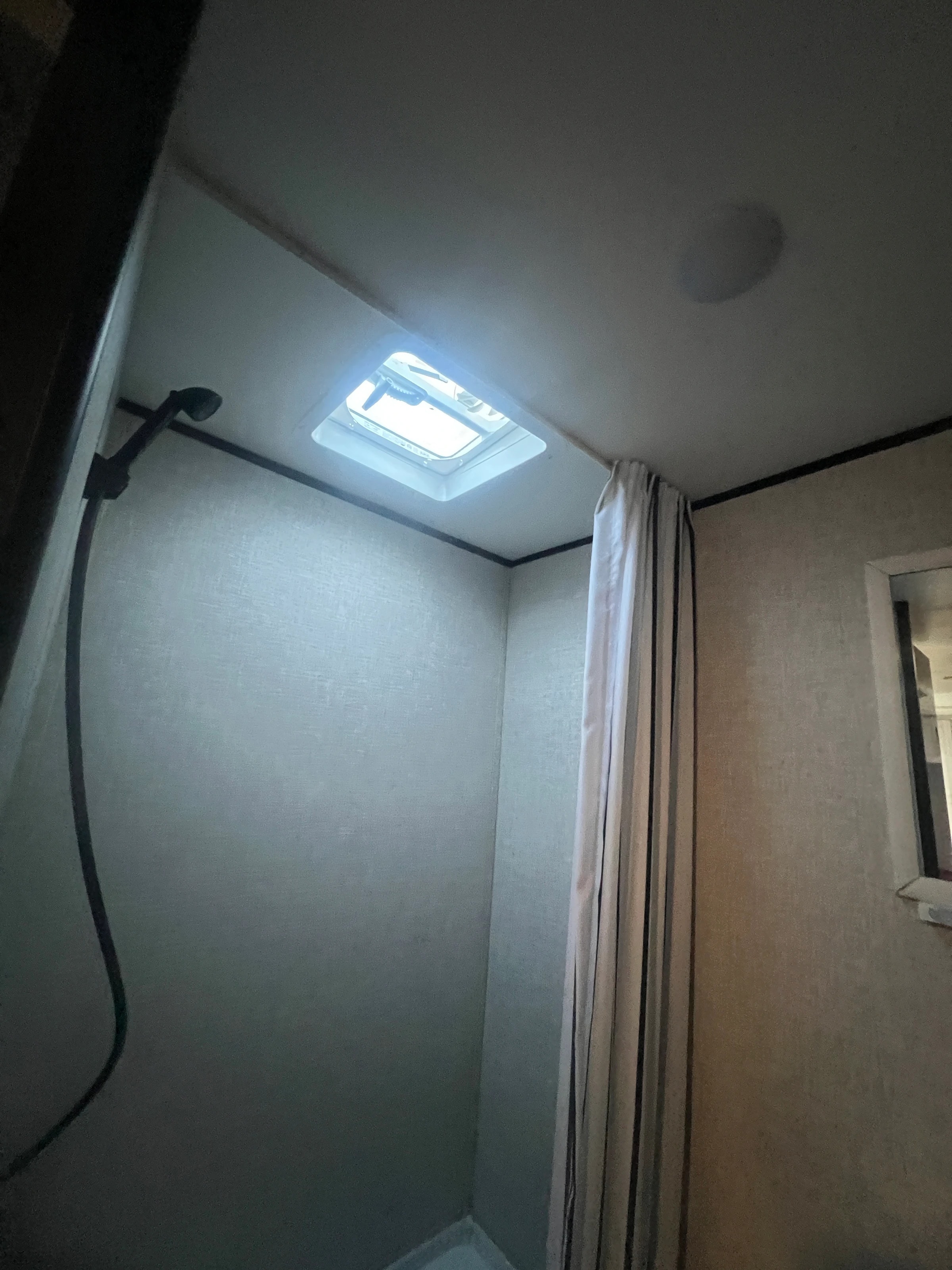 Shower stall with an overhead skylight and a pull-across curtain