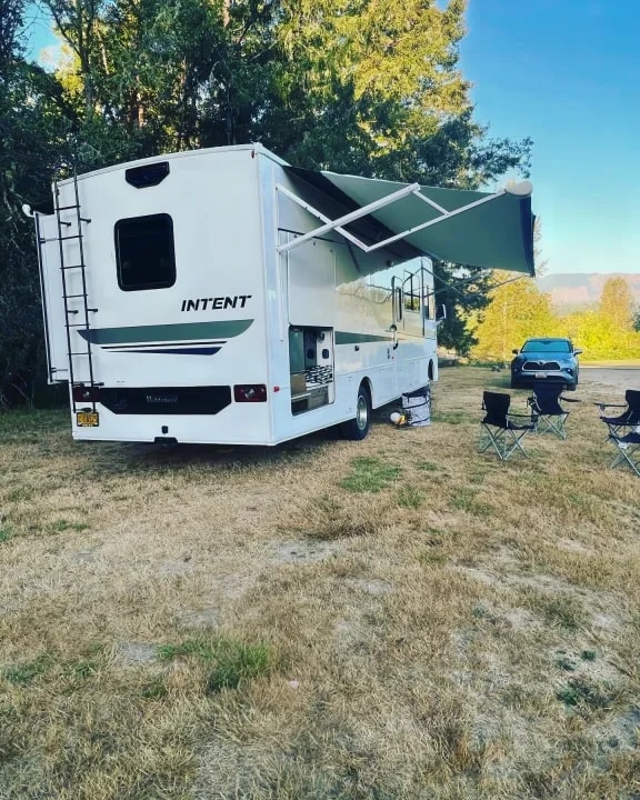 Rear three-quarter view of the motorhome with awning extended and camp chairs set up