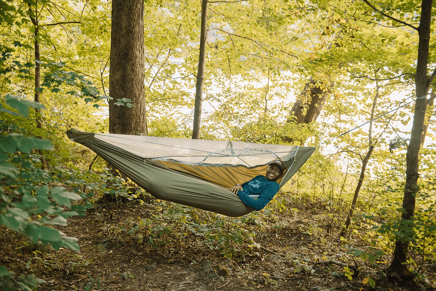 Camper lying in an olive hammock with a bug net strung between trees