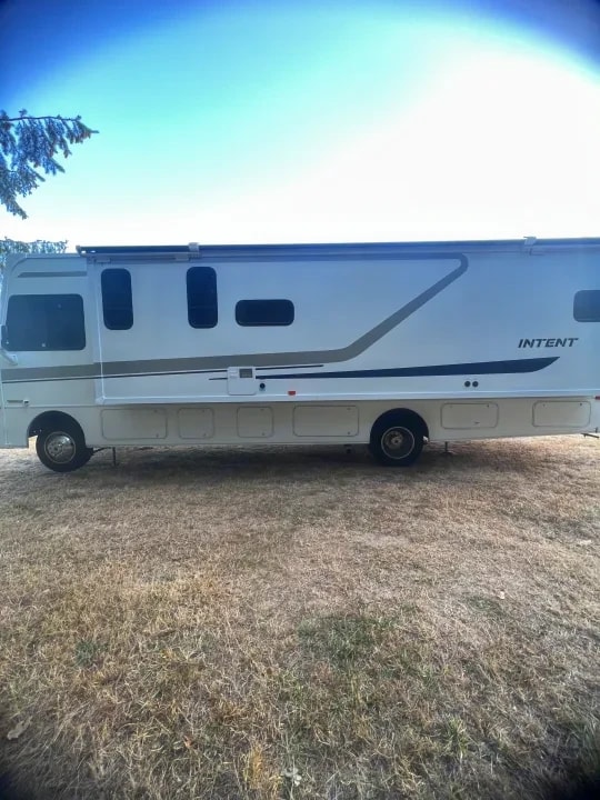 Full side profile of the motorhome parked on dry grass with clear sky
