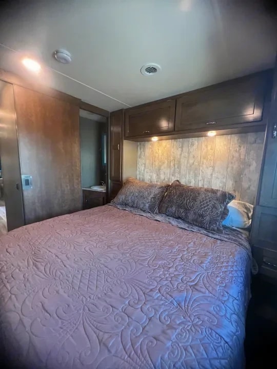 Bedroom with queen bed in pink quilted bedding and overhead cabinets
