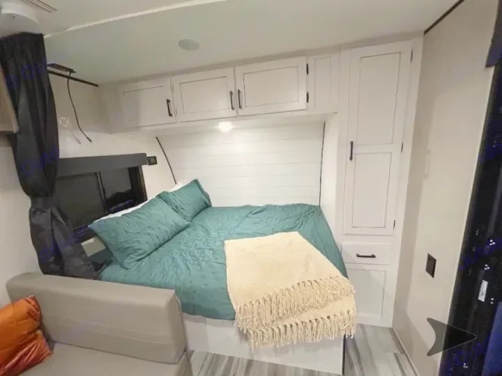 Queen bed with teal bedding and overhead storage cabinets