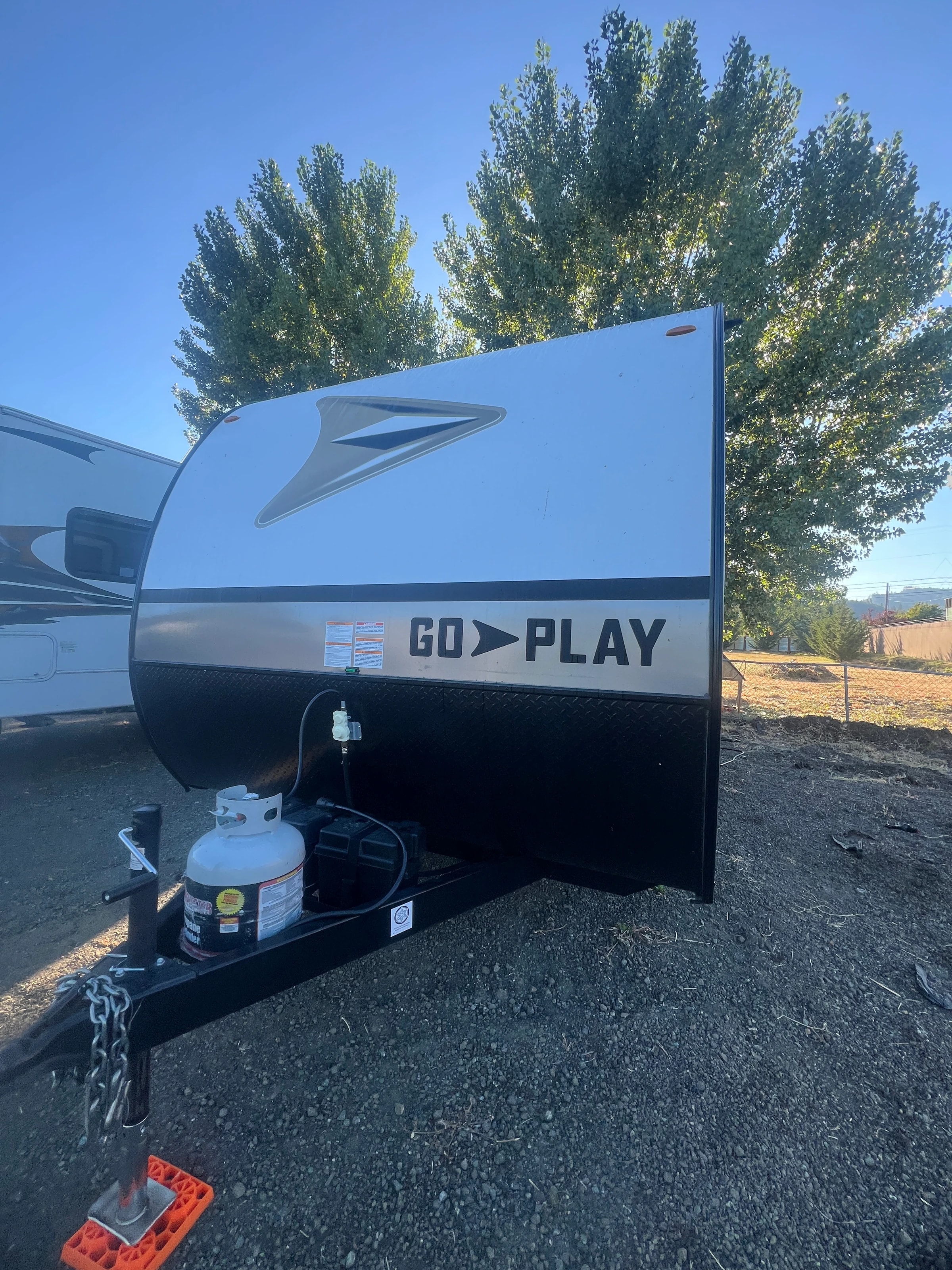 Front of the trailer with its propane tank and coupler, parked on gravel