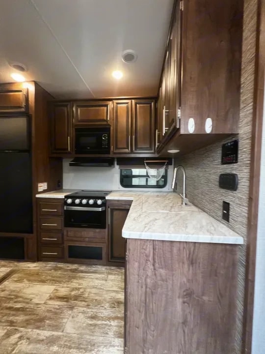 Kitchen with wood cabinetry, microwave, range, and stone-look countertop