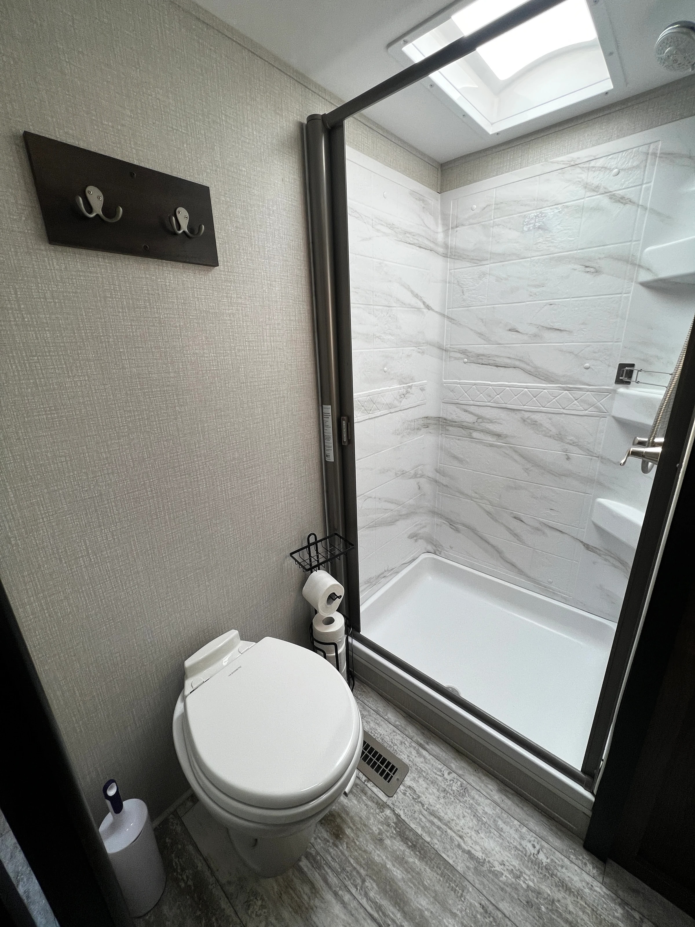 Bathroom with glass-door shower stall, marble-look surround, and toilet